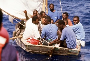 Haitian refugees watch from their crowded sailboat as a U.S. Coast Guard vessel approaches.  Nearly 15,000 Haitians have been intercepted and brought aboard Navy and Coast Guard ships between October and December 1991.  They are then transported to Naval Station, Guantanamo Bay, Cuba, for temporary housing until their legal status has been determined.