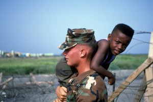 Marine LCPL Donald Kenley, Camp Lejuene, North Carolina carries one of the Haitian refugee children at the Camp McCalla tent facilities on the U.S. Naval Base at Guantanamo Bay, Cuba.   More than 14,000 refugees attempted to reach the United States by boat and were picked up by the Coast Guard in international waters and transported to the base at Guantanamo Bay. Exact Date Shot Unknown.