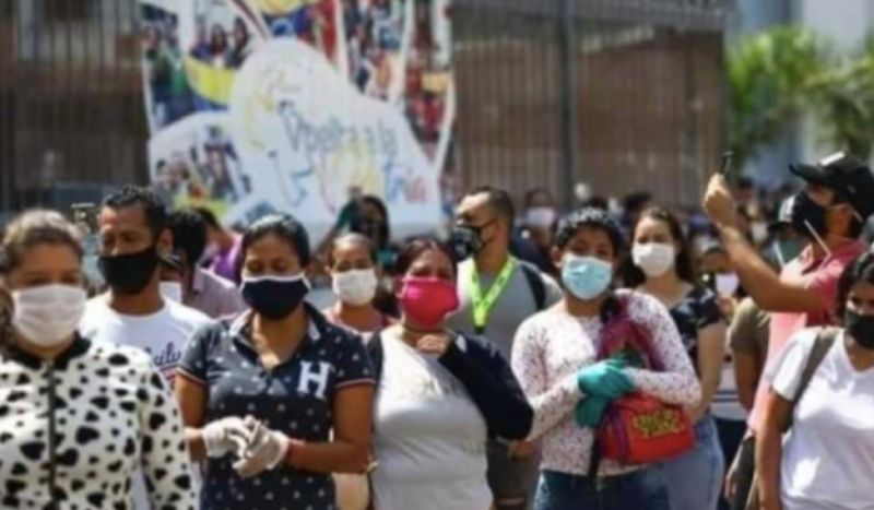 This is a color photograph of a group of people outside on a sunny day wearing masks.
