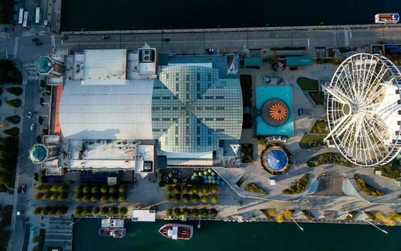 The Navy Pier building, including the Museum, is bordered on the top and left by streets and the bottom by water. The two towers of the Pier building are on the left and the Centennial Wheel is on the right.