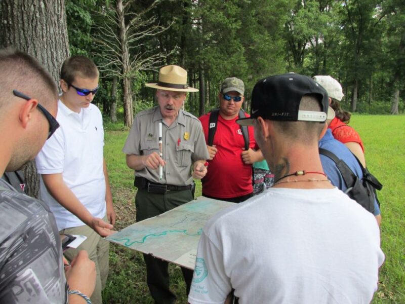 A group of people consults a map while a park ranger addresses them. 