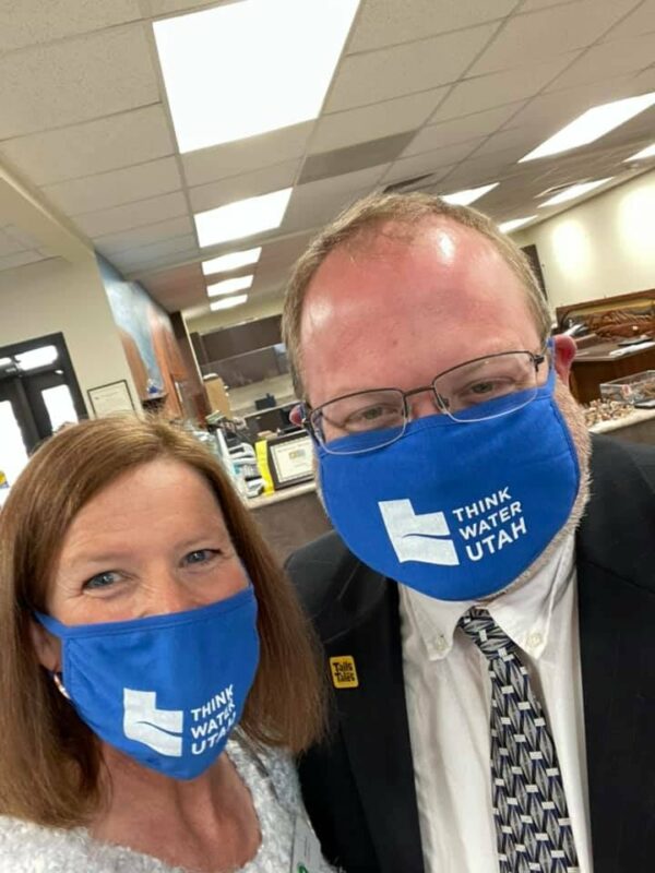 Two people smile wearing blue masks with the words "Think Water Utah" look into the camera with smiling eyes.