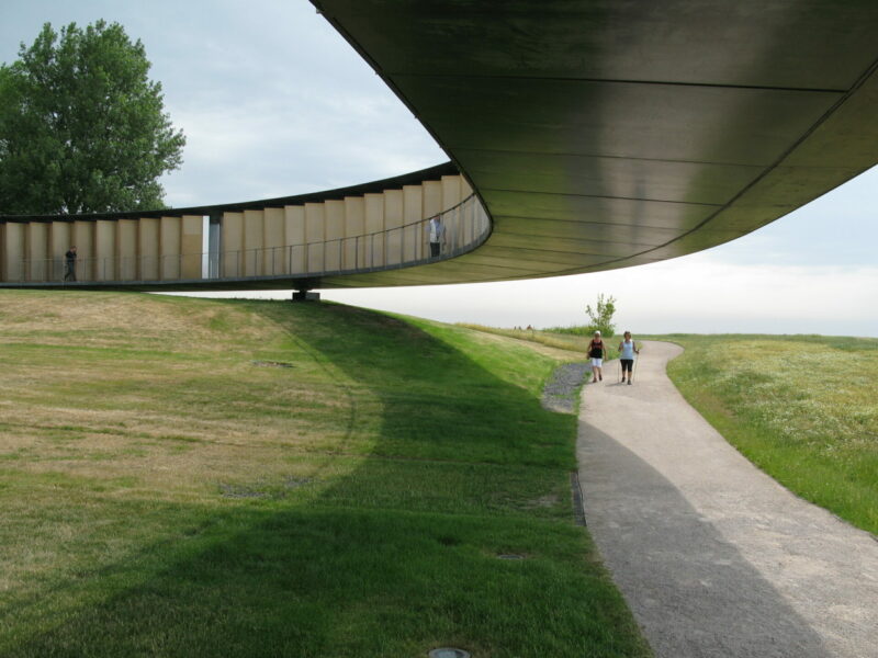 Circular monument made of metal on top of grass and a concrete walkway. Two people walk under the monument.