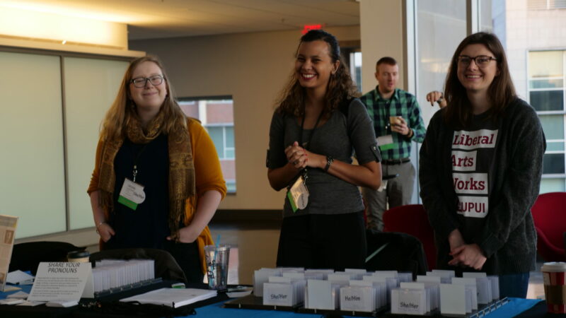 three IUPUI students behind a registration desk distributing badges for symposium participants.