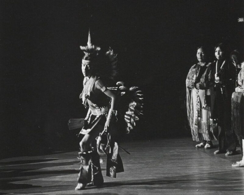 A member of the Na Rhma Wa Ci American Indian Dancers performs with other ensemble members looking on.