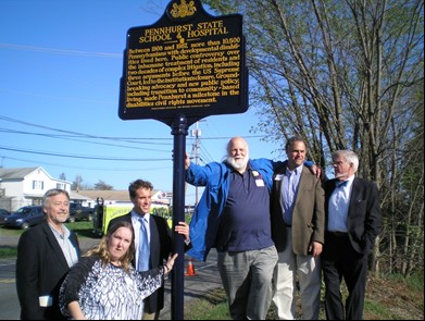 Six white people, 5 men and 1 woman, are standing beside a 10 feet tall sign.