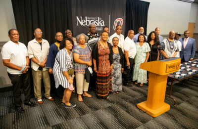 The Omaha 54 group stands in front of the University of Nebraska-Omaha banner