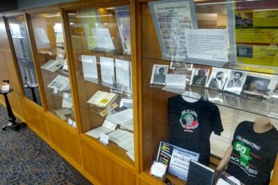 A selection of artifacts, including documents, tshirts, and photographs, in an exhibit case. 