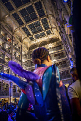 Back of person in purple and blue costume with wings. Camera angled upward toward soaring ceiling of library.