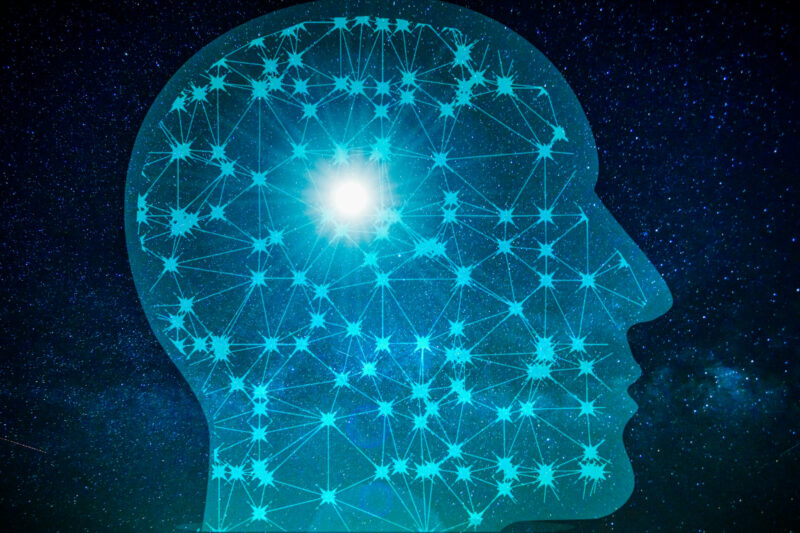 Outline of a human head against a dark background depicting stars and galaxies. Inside the outline of the head is a matrix of stars that are connected to one another by lines and a bright glowing star in the background.