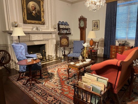 Photograph of the Indiana Period Room at the DAR museum. It is set up as a formal living room, with a large fireplace on one wall. Various pieces of furniture such as a sofa, chairs, coffee table, and magazine rack.