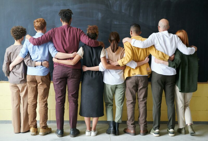 People of various genders and races standing arm in arm 