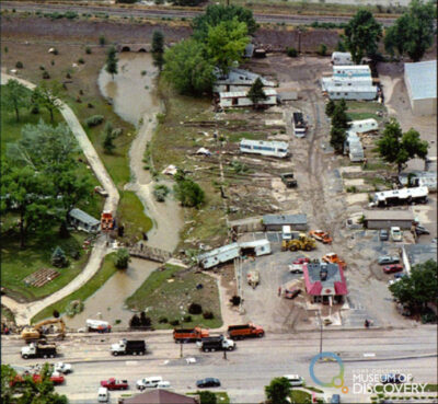 Aerial view of trailer park destruction with trailers askew near trees, a road, and greenspace.