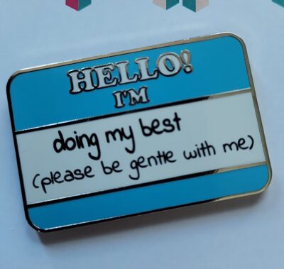Blue and white striped "introduction" pin that reads: "Hello! I'm..." and in a font that appears handwritten, "doing my best (please be gentle with me)"