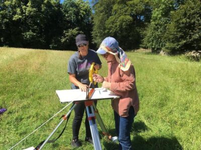 Two students engaged in plane table mapping stand in a grassy field.