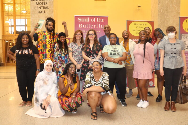 Fifteen people pose in front of an exhibit. The words "Soul of the Butterfly," appear behind them.