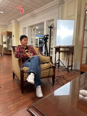 Susan in a chair with a video camera and lighting equipment behind her.