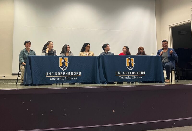 Eight panelists sitting behind a table hosting a discussion.